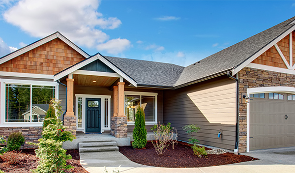 Home exterior showing a mix of horizontal lap siding, cedar shakes, and stacked stone wainscoting with front yard landscaping and a concrete pathway